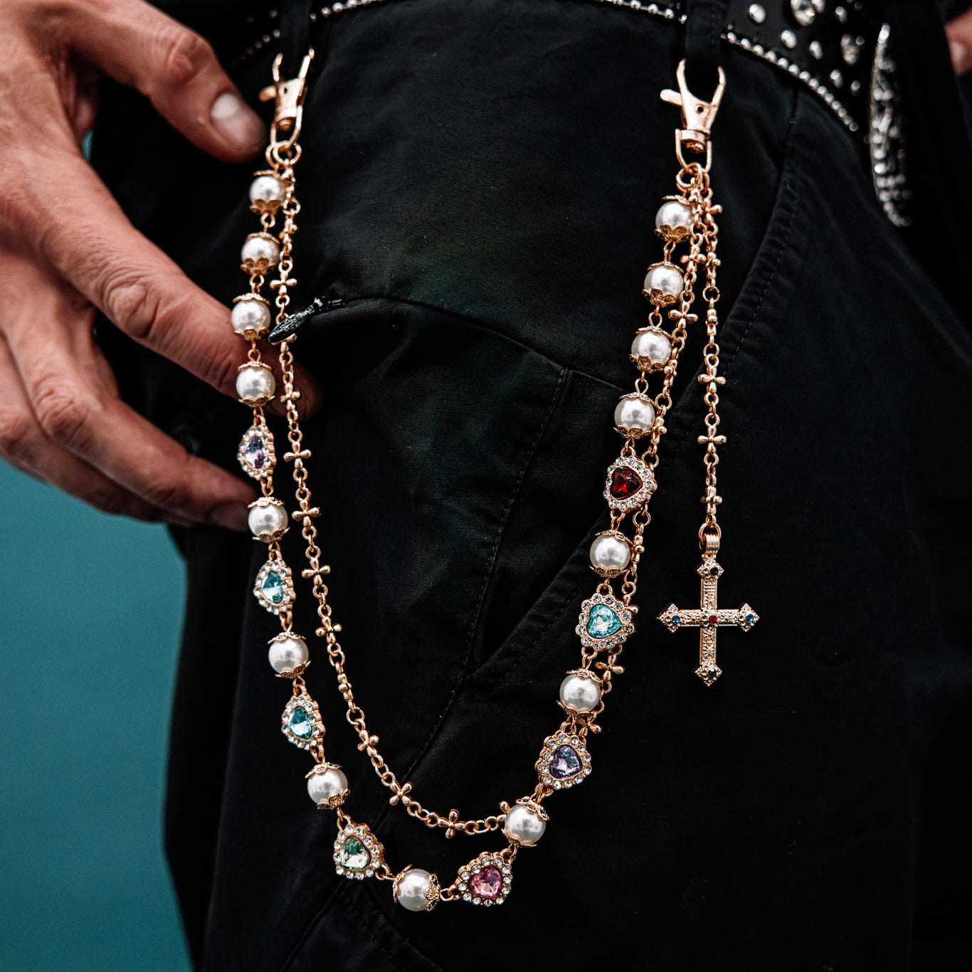 Close-up of a decorative belt with a rosary and cross details on a dark background