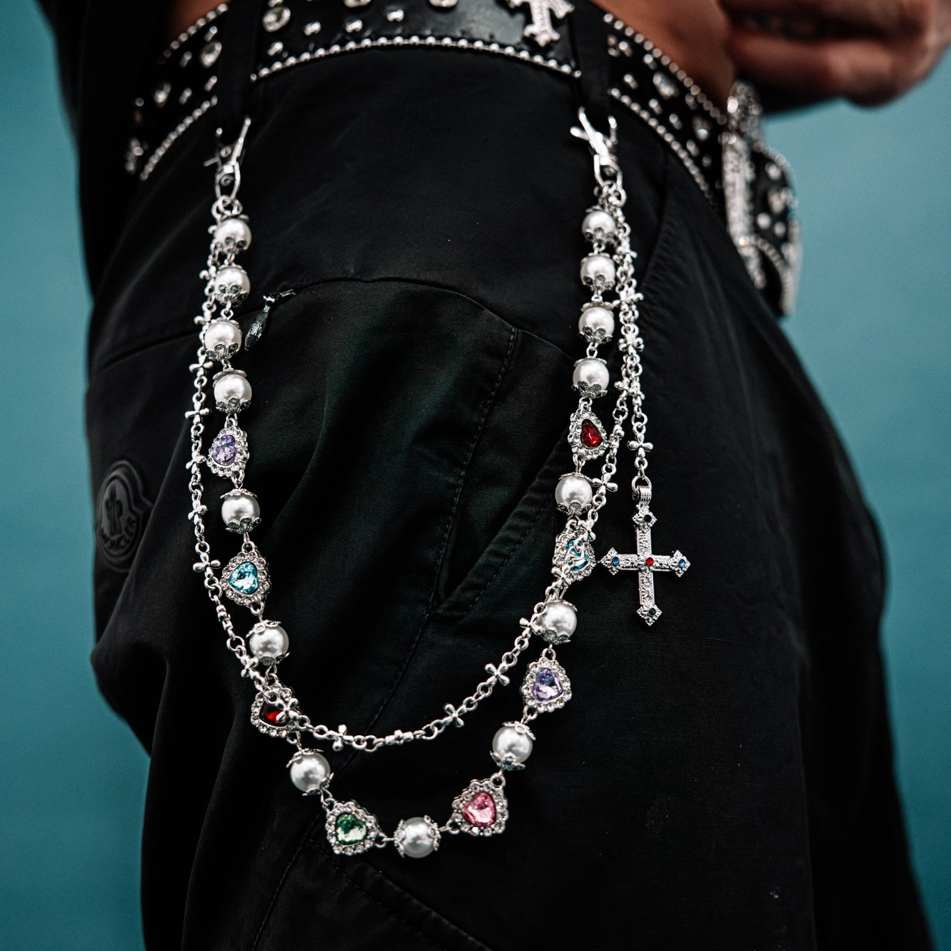 Close-up of a person wearing a decorative belt with beads and crosses, against a dark background.