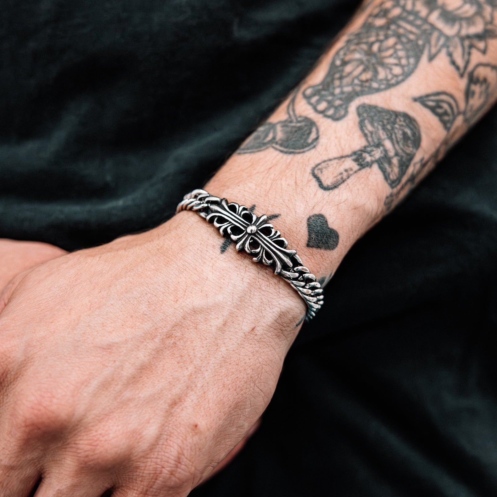 Silver bracelet on a wrist with tattoos against a dark background