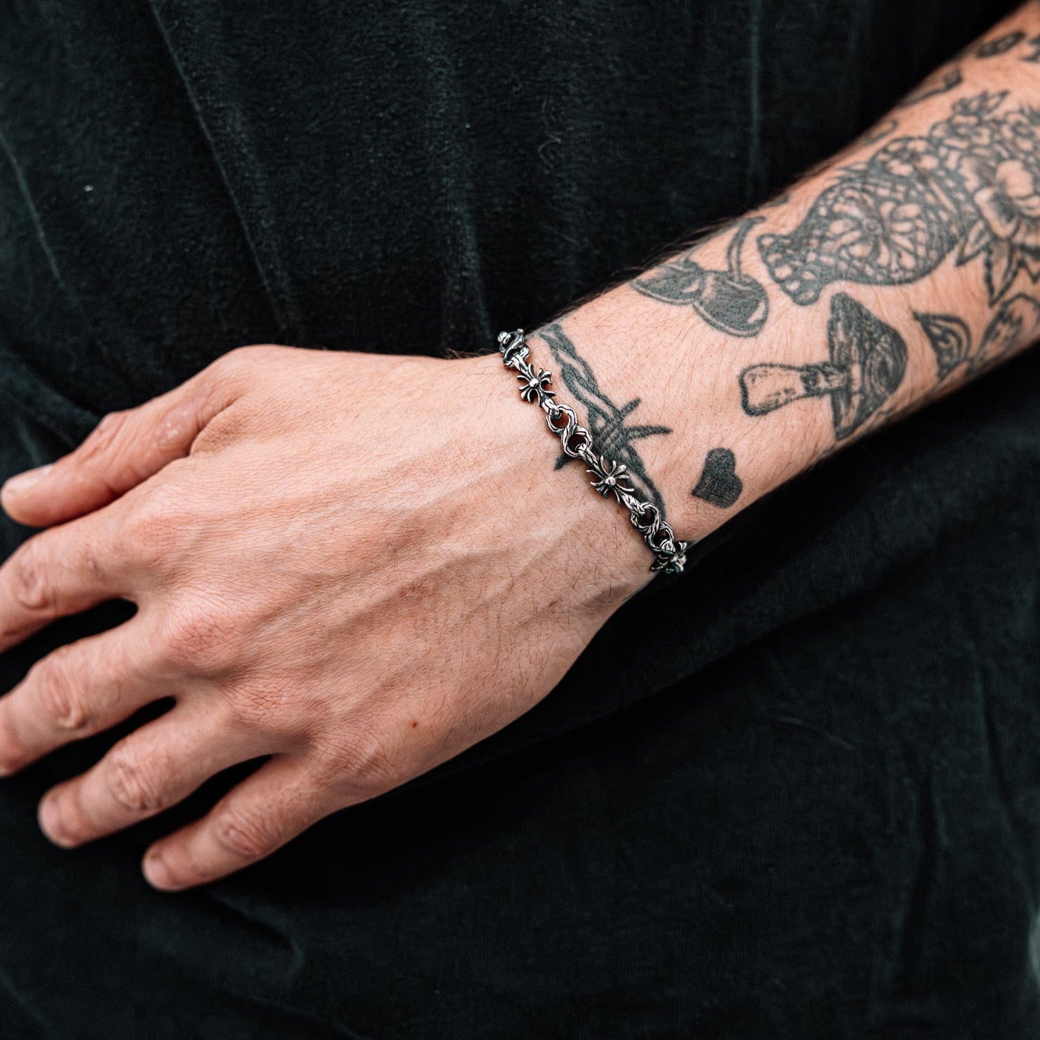 Person wearing a bracelet with tattoos on their arm against a black background