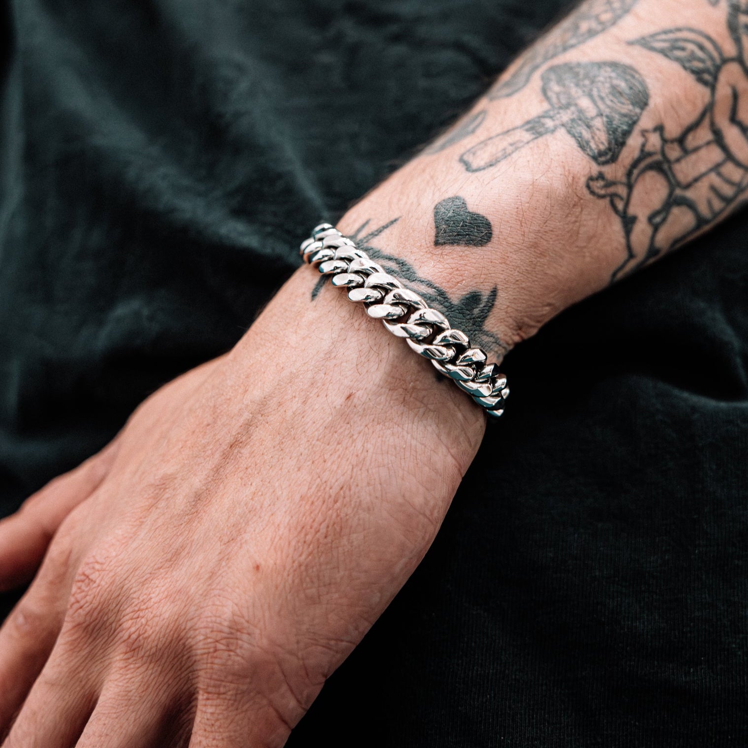 Silver chain bracelet on a wrist with tattoos against a dark background