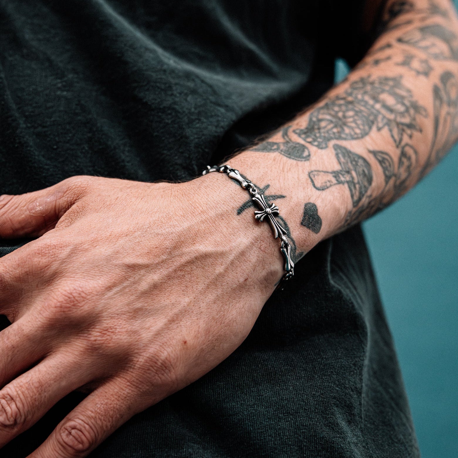 Person wearing a silver bracelet with tattoos on their arm against a dark background