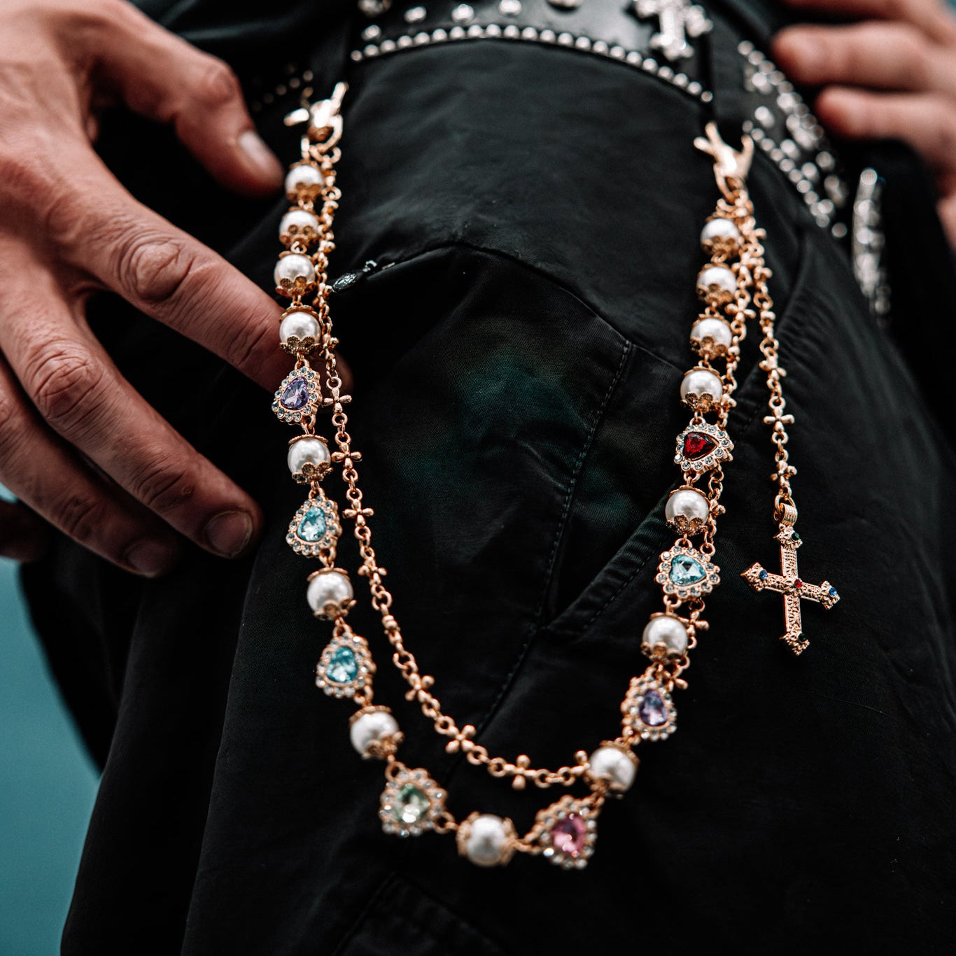 Close-up of a person wearing a black jacket with studded details, focusing on a gold chain necklace.