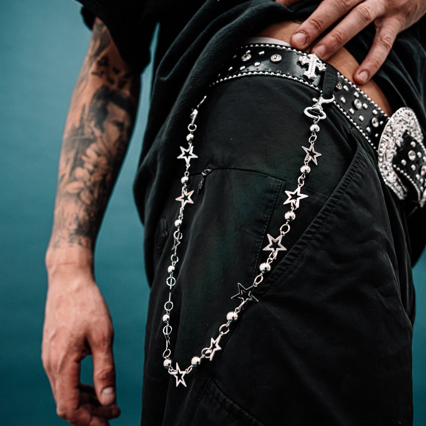 Person wearing a black outfit with decorative chains and patterns on a blue background